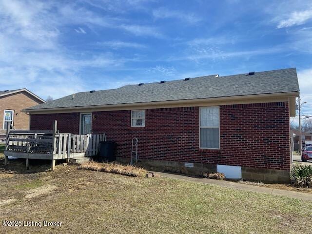 rear view of property with a yard, brick siding, roof with shingles, and a wooden deck