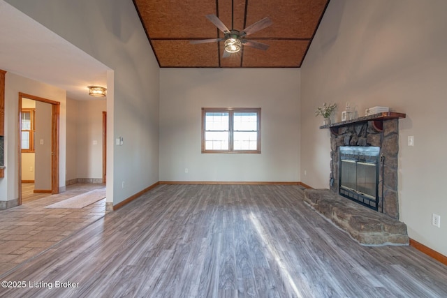 unfurnished living room featuring a stone fireplace, ceiling fan, light hardwood / wood-style floors, and lofted ceiling