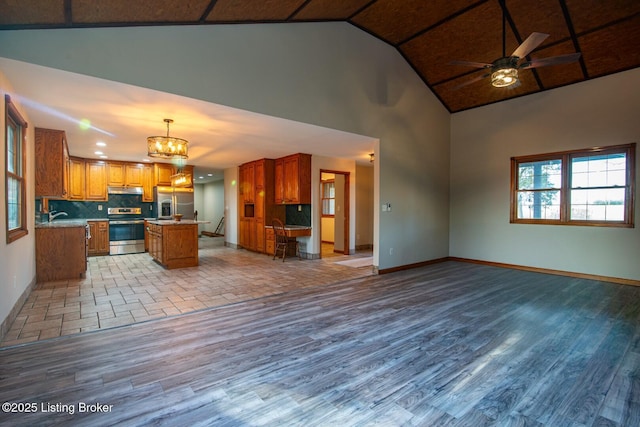 kitchen with a center island, stainless steel appliances, tasteful backsplash, decorative light fixtures, and ceiling fan with notable chandelier