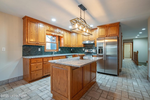 kitchen featuring appliances with stainless steel finishes, backsplash, light stone counters, decorative light fixtures, and a kitchen island