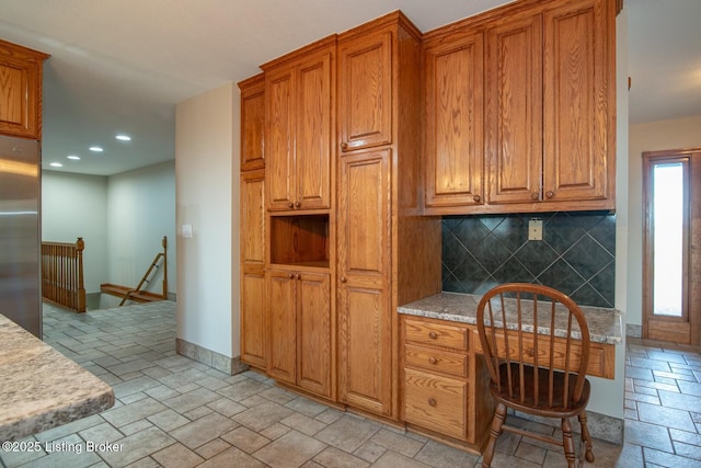 kitchen with built in desk, backsplash, and stainless steel refrigerator