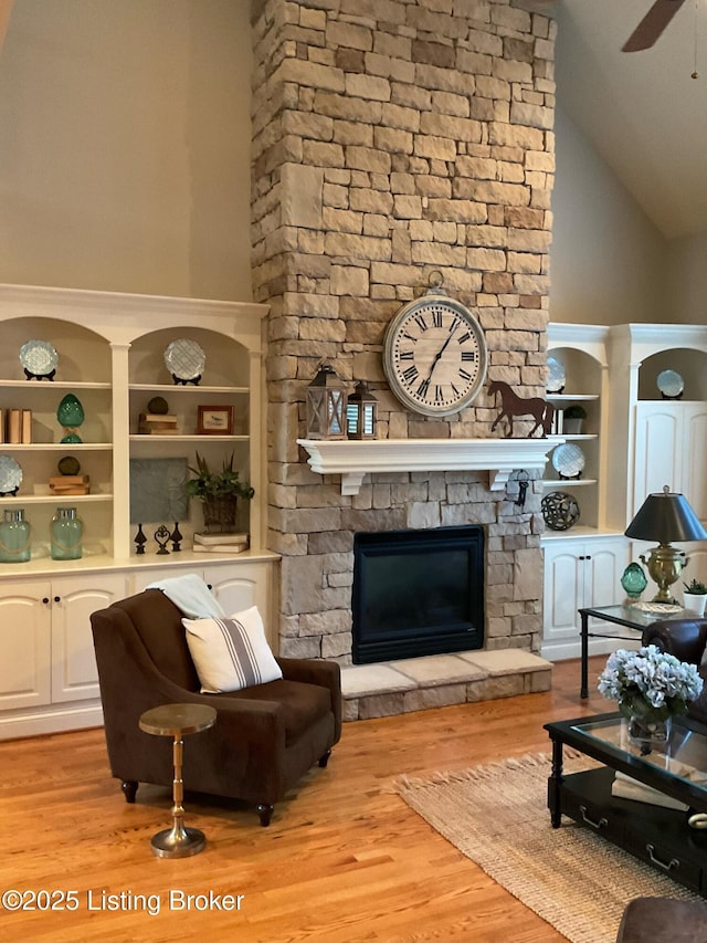 living room featuring ceiling fan, light wood-type flooring, a fireplace, built in shelves, and high vaulted ceiling