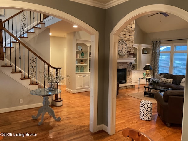 living room with crown molding, built in features, light hardwood / wood-style floors, and a fireplace