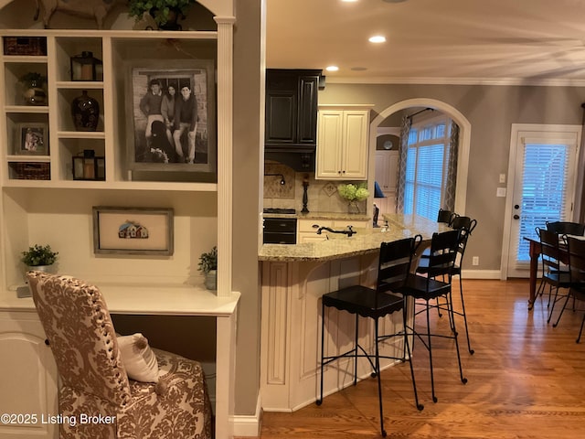 bar with light stone countertops, wall oven, tasteful backsplash, ornamental molding, and dark wood-type flooring