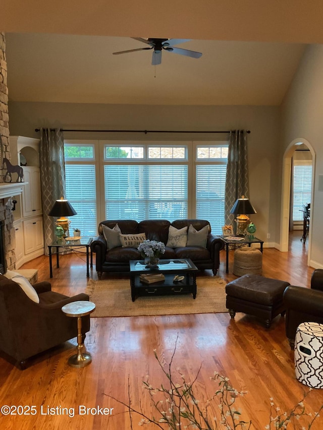 living room with ceiling fan, hardwood / wood-style floors, lofted ceiling, and a stone fireplace