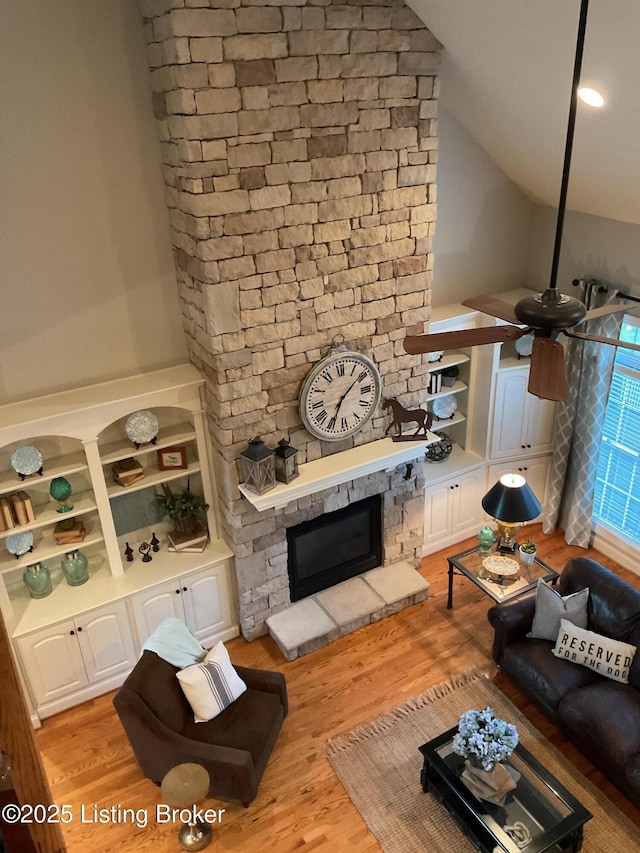 living room with built in features, light hardwood / wood-style flooring, a fireplace, and lofted ceiling