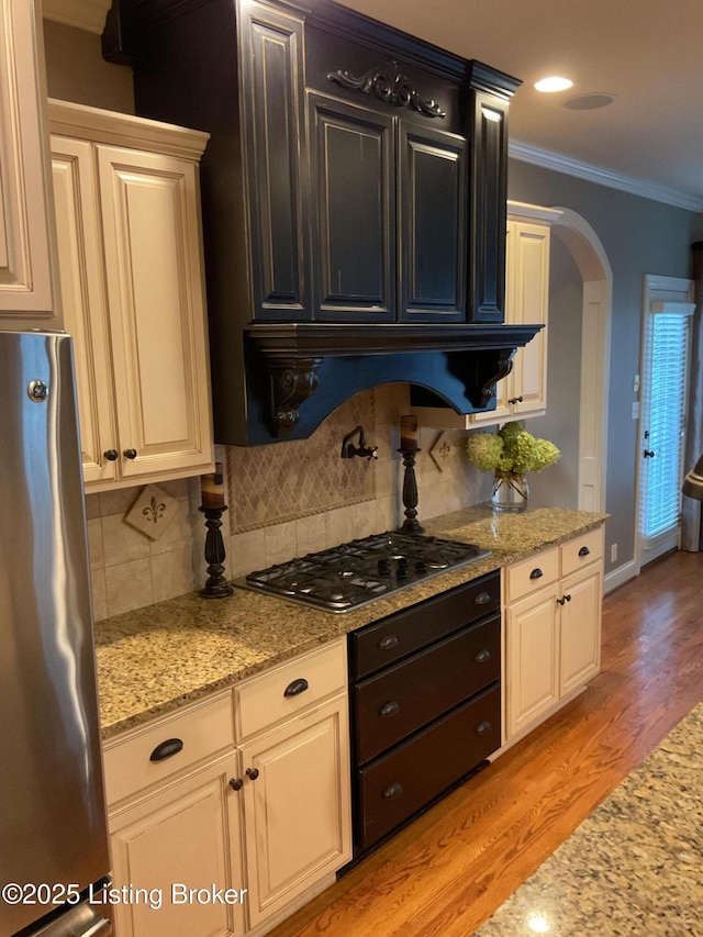 kitchen featuring appliances with stainless steel finishes, light wood-type flooring, tasteful backsplash, light stone counters, and ornamental molding