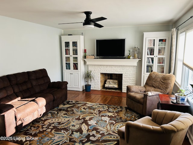 living room featuring ceiling fan, dark hardwood / wood-style flooring, and a brick fireplace