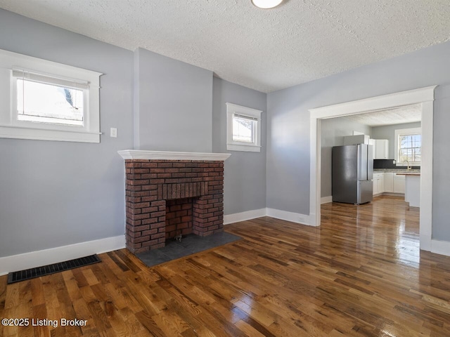 unfurnished living room with a brick fireplace, a textured ceiling, a healthy amount of sunlight, and dark wood-type flooring