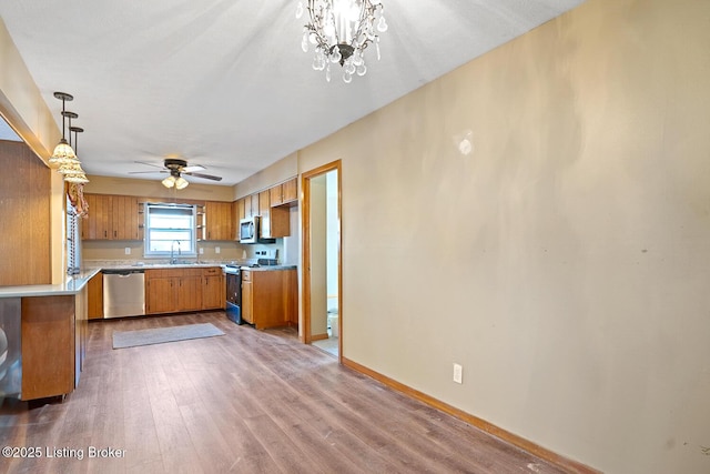 kitchen featuring sink, hardwood / wood-style flooring, appliances with stainless steel finishes, hanging light fixtures, and ceiling fan with notable chandelier