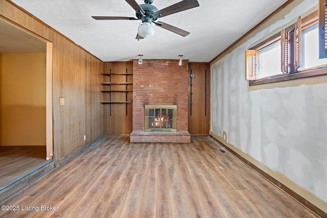 unfurnished living room featuring a textured ceiling, ornamental molding, wooden walls, a fireplace, and hardwood / wood-style floors