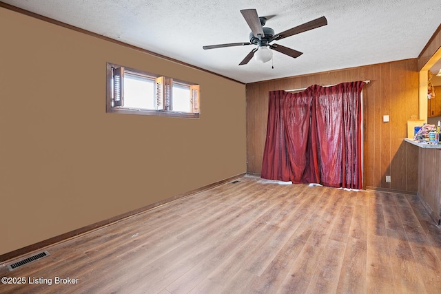 unfurnished room with ceiling fan, wood walls, a textured ceiling, and light wood-type flooring