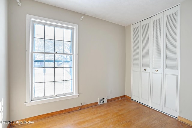 unfurnished bedroom with multiple windows, light wood-type flooring, and a closet