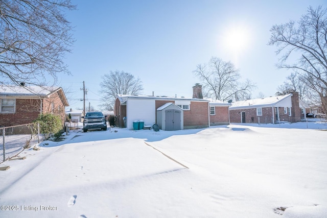 snow covered back of property featuring a shed