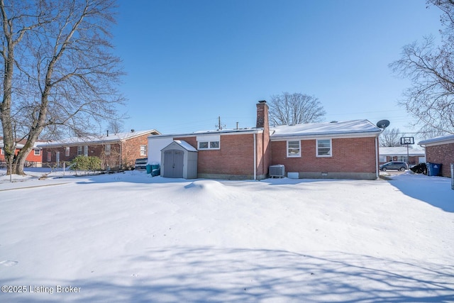 snow covered back of property featuring central AC unit and a shed