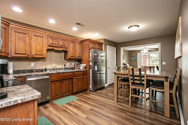 kitchen featuring appliances with stainless steel finishes, hardwood / wood-style floors, sink, backsplash, and light stone countertops