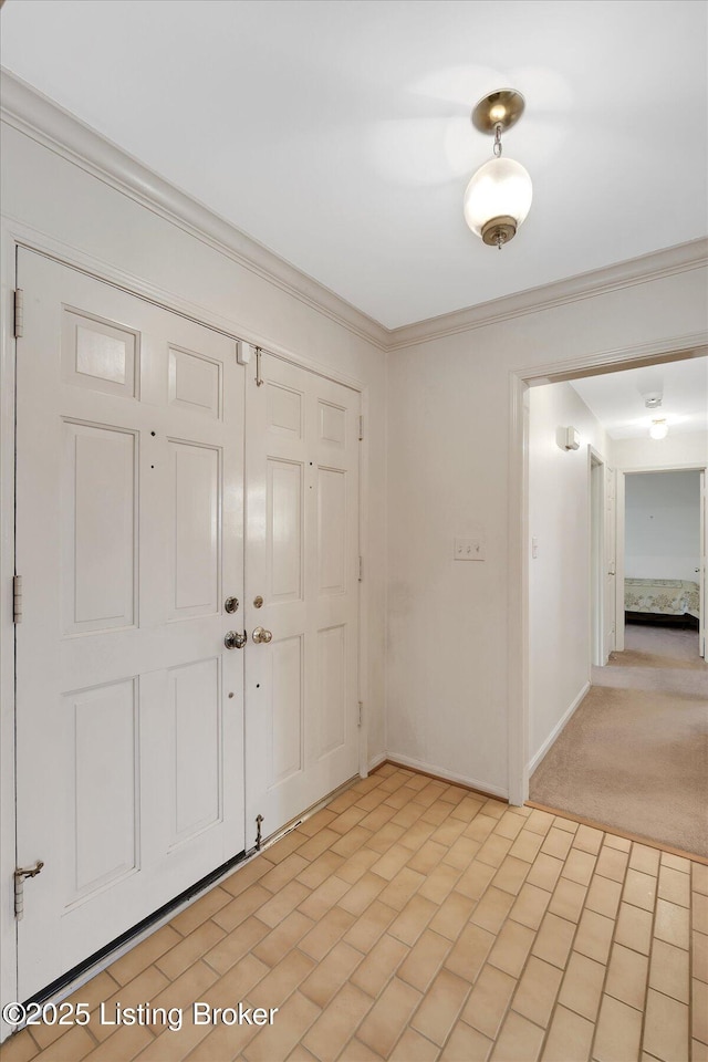 foyer featuring crown molding, baseboards, and light carpet