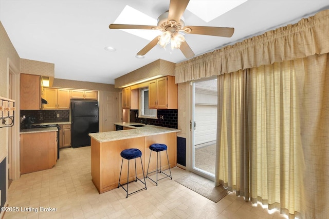 kitchen with a peninsula, a skylight, freestanding refrigerator, a sink, and light countertops