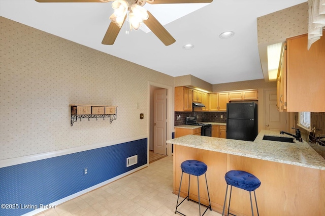 kitchen featuring wallpapered walls, under cabinet range hood, a peninsula, black appliances, and a sink