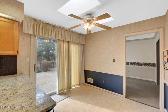 interior space featuring baseboards, visible vents, wallpapered walls, a skylight, and ceiling fan