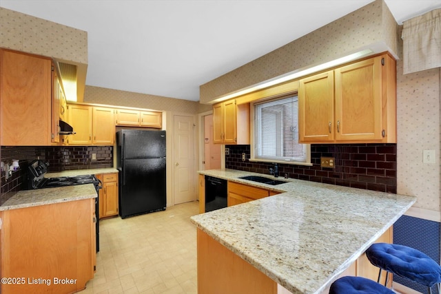 kitchen with black appliances, a sink, under cabinet range hood, a peninsula, and wallpapered walls