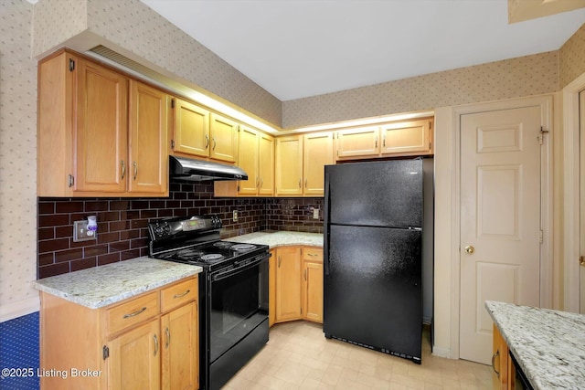 kitchen featuring backsplash, wallpapered walls, under cabinet range hood, light stone counters, and black appliances