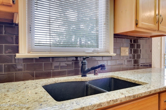 kitchen featuring decorative backsplash, light stone countertops, light brown cabinets, and a sink