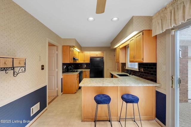 kitchen with wallpapered walls, light countertops, a peninsula, black appliances, and a sink