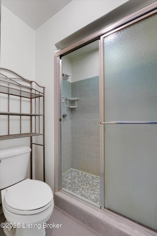 bathroom with tile patterned floors, toilet, and a stall shower