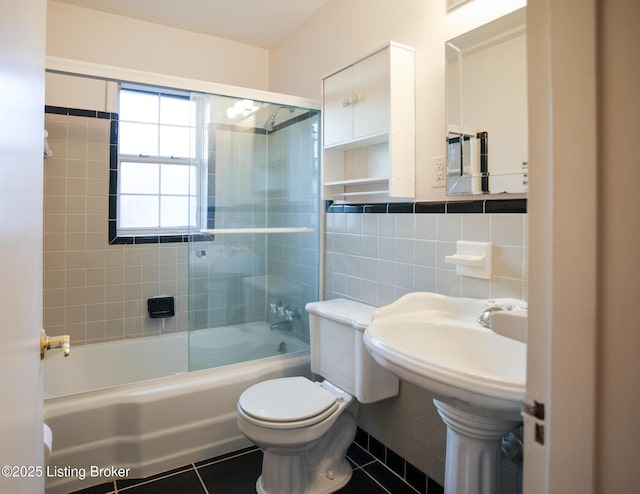 bathroom featuring toilet, tile patterned floors, tile walls, and bath / shower combo with glass door