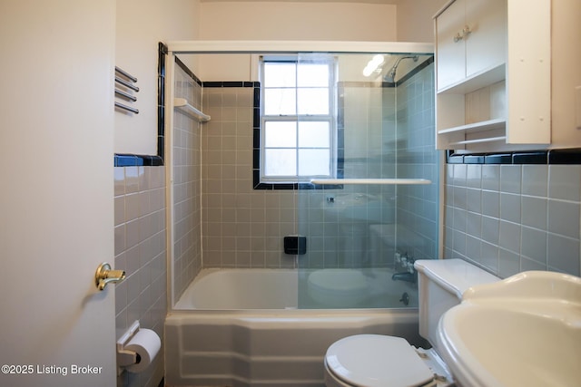 full bathroom featuring combined bath / shower with glass door, tile walls, sink, and toilet