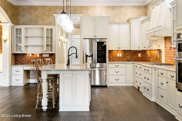 kitchen featuring appliances with stainless steel finishes, premium range hood, light stone counters, decorative light fixtures, and a center island with sink