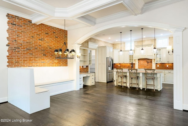 interior space with white cabinetry, stainless steel fridge with ice dispenser, decorative light fixtures, a kitchen island with sink, and a breakfast bar