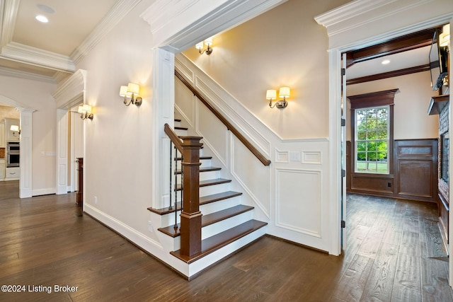 staircase with hardwood / wood-style floors, a stone fireplace, and crown molding