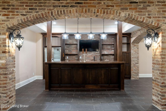 bar featuring dark brown cabinetry, pendant lighting, brick wall, and ornamental molding