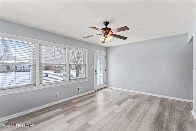 empty room featuring ceiling fan, plenty of natural light, light hardwood / wood-style floors, and a textured ceiling