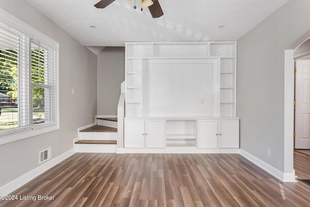 unfurnished living room featuring built in shelves, ceiling fan, and dark hardwood / wood-style flooring