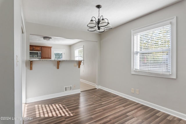 unfurnished dining area featuring a textured ceiling, dark hardwood / wood-style flooring, and an inviting chandelier