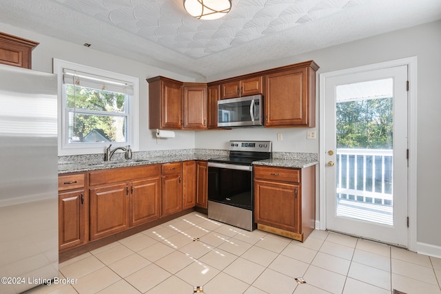 kitchen with a wealth of natural light, sink, light stone counters, a textured ceiling, and appliances with stainless steel finishes