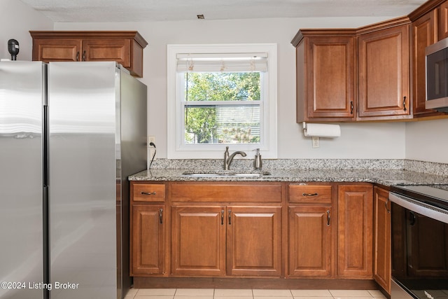 kitchen with light stone countertops, stainless steel appliances, light tile patterned flooring, and sink