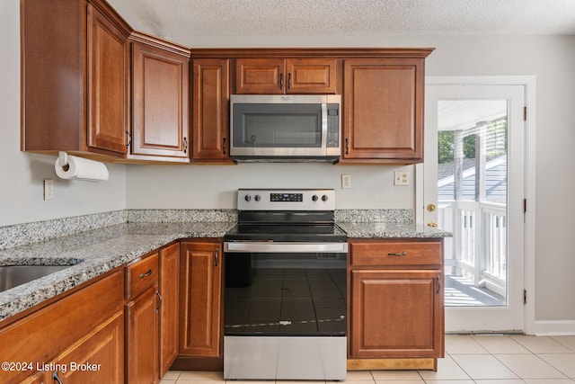 kitchen with a healthy amount of sunlight, light stone countertops, light tile patterned floors, and stainless steel appliances