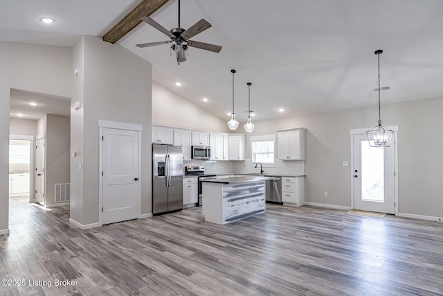 kitchen with stainless steel appliances, beam ceiling, white cabinets, and pendant lighting