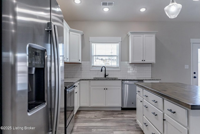 kitchen with stainless steel appliances, decorative backsplash, light wood-type flooring, white cabinets, and sink