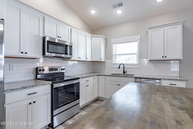 kitchen with light stone counters, stainless steel appliances, lofted ceiling, white cabinets, and sink