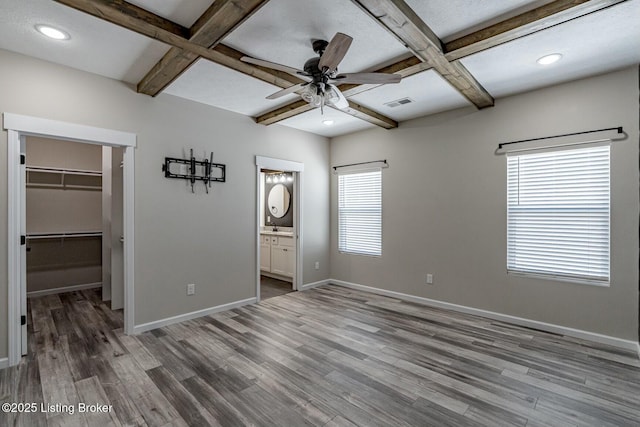 unfurnished bedroom with a walk in closet, a closet, coffered ceiling, and multiple windows