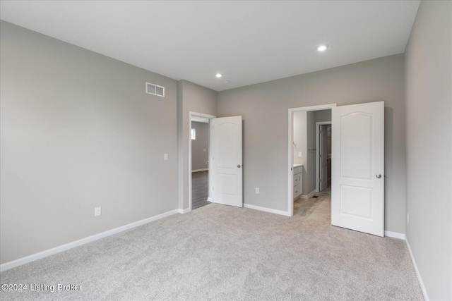 unfurnished bedroom with ensuite bathroom and light colored carpet