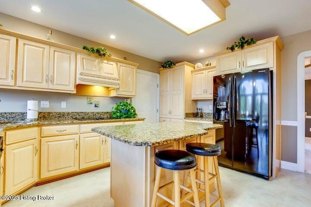 kitchen featuring black appliances, a kitchen breakfast bar, light stone countertops, light brown cabinetry, and a kitchen island