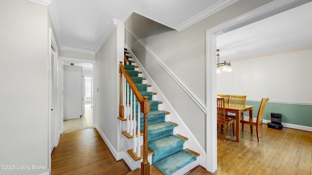 staircase featuring hardwood / wood-style floors, an inviting chandelier, and ornamental molding