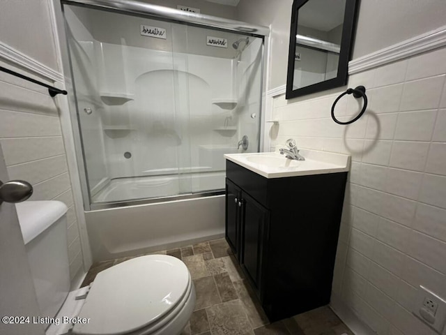 full bathroom with toilet, vanity, tile walls, and combined bath / shower with glass door