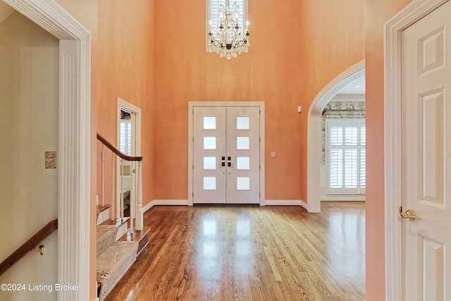 entrance foyer featuring a towering ceiling, wood-type flooring, ornamental molding, and a chandelier